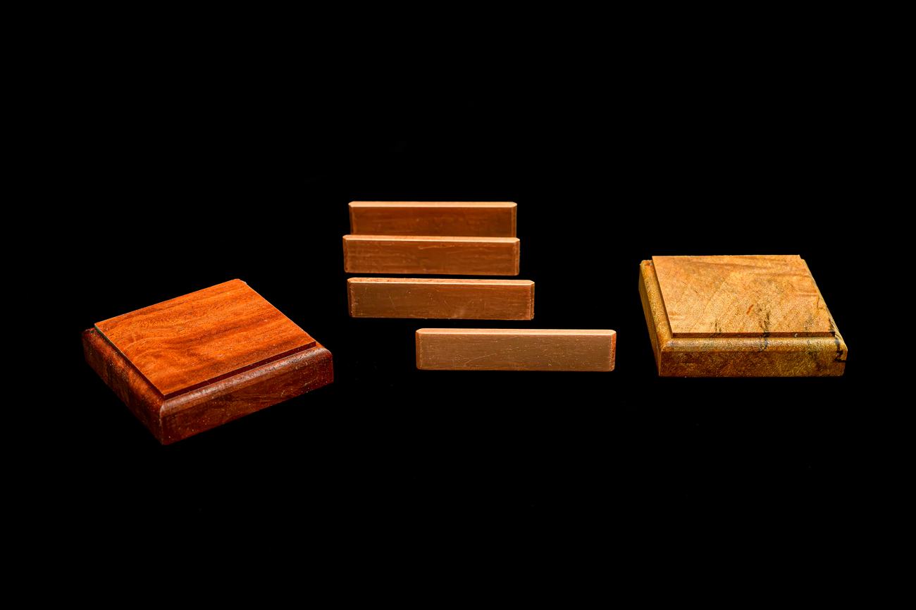 A single Jarrah tile, a single rose myrtle tile, and four lengths of copper spline, laid out before assembly