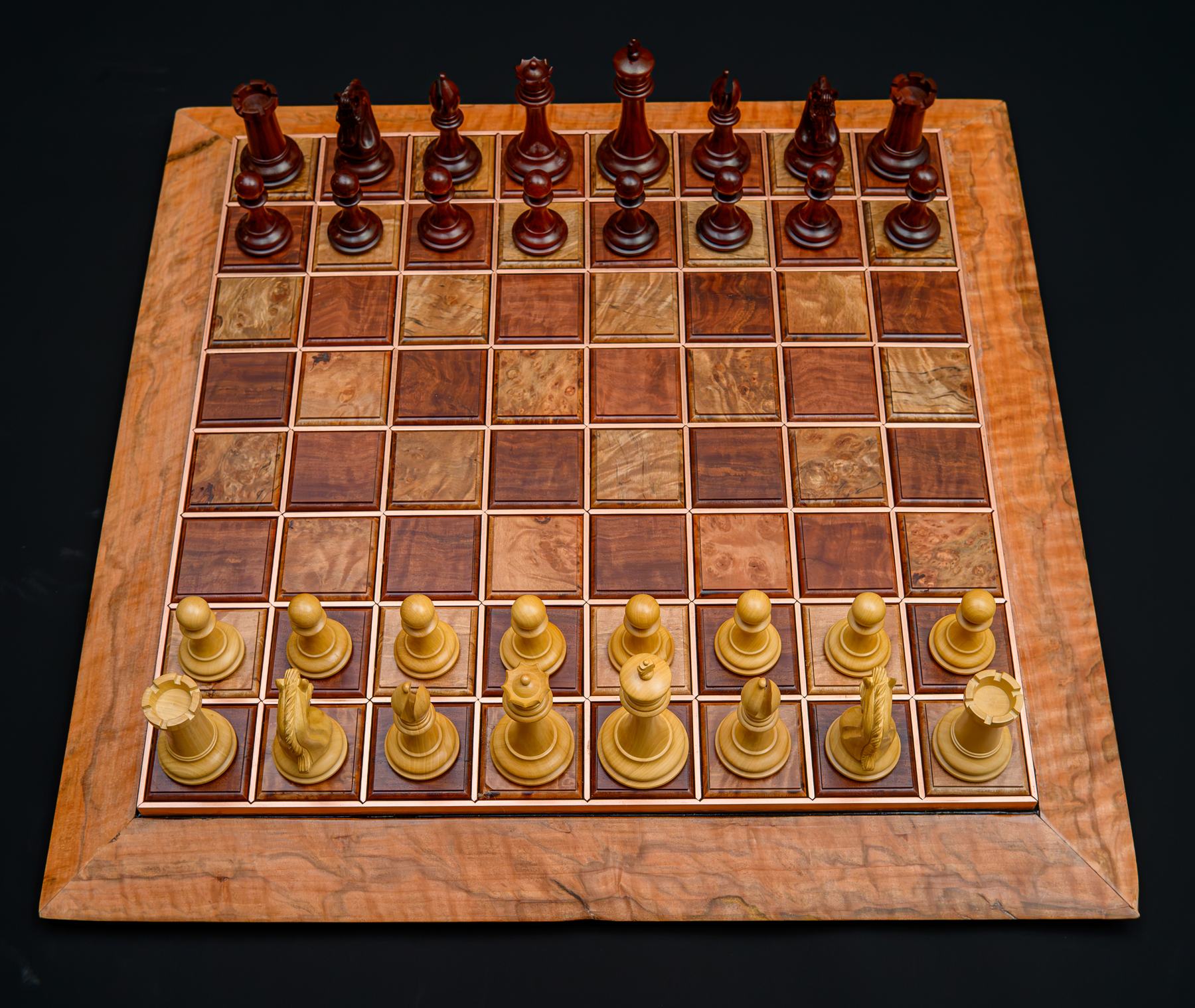 A full set of dark and light chess pieces arrayed on a Jarrah and Tasmanian Rose Myrtle board